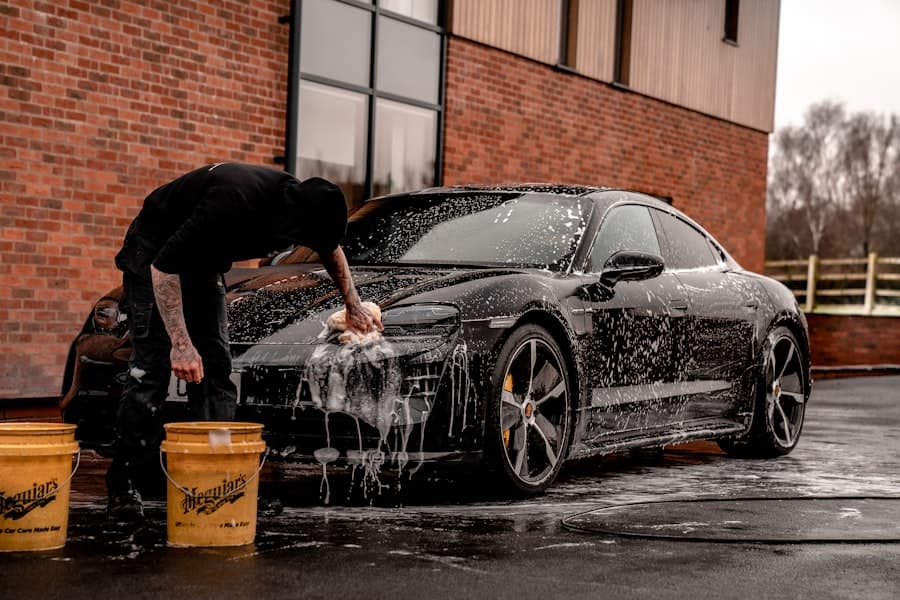 Detailer hand-washing a black car covered in soap suds